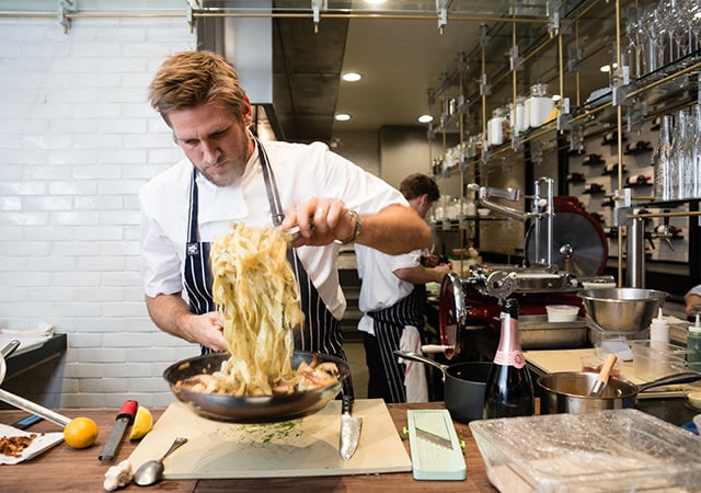 Chef Curtis Stone twirling pasta in a pan